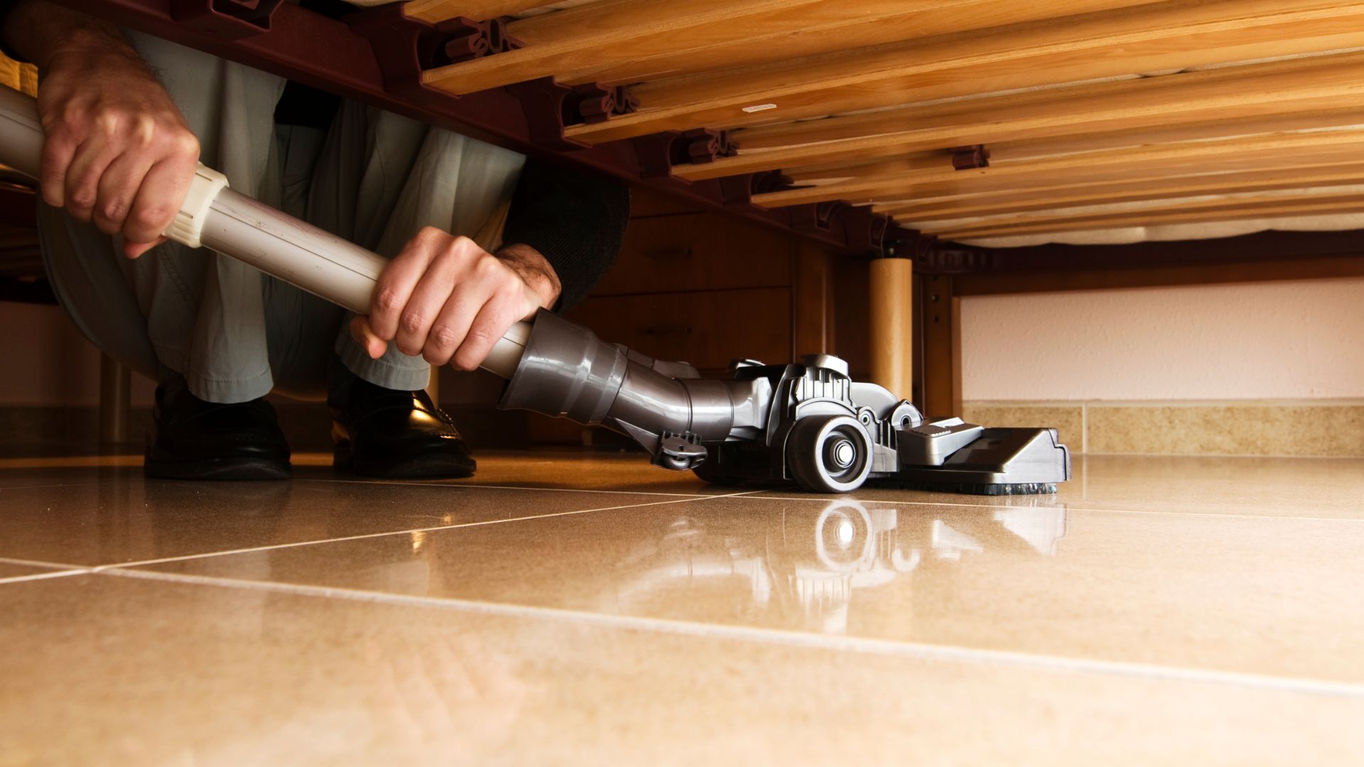 Hands using a vacuum cleaner on a shiny hardwood floor