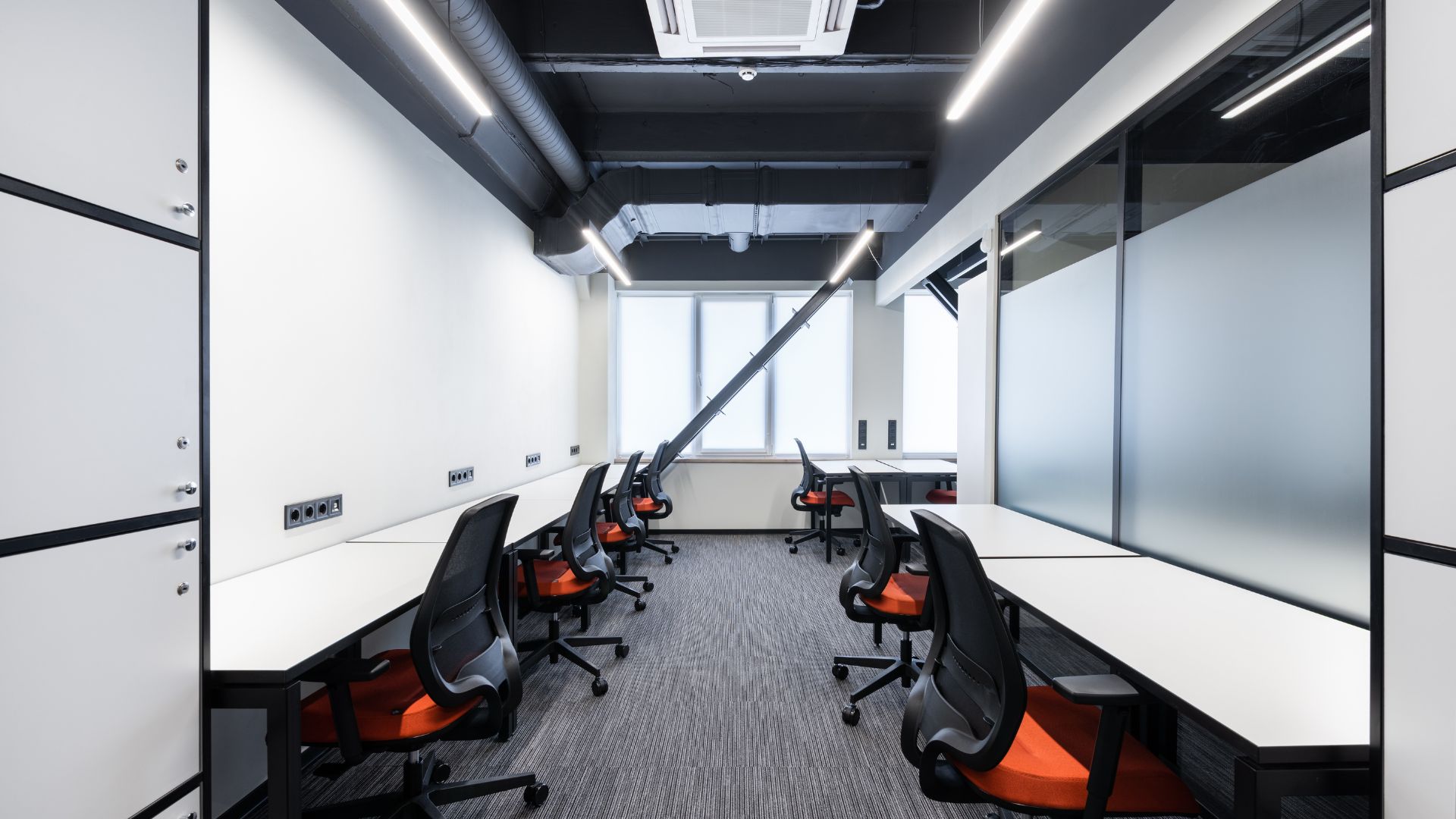 Modern office workspace with black and orange chairs and exposed ceiling