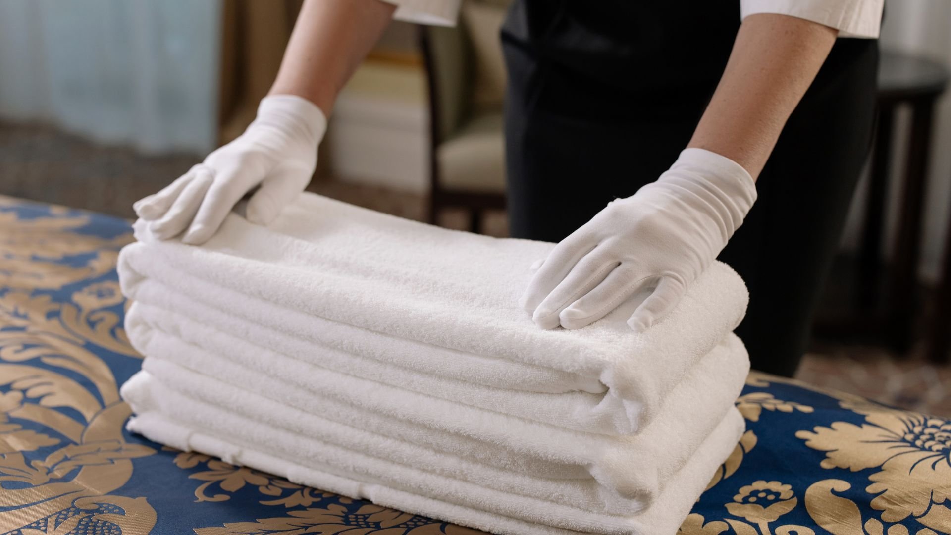 Gloved hands neatly folding clean white towels on a decorative blue surface