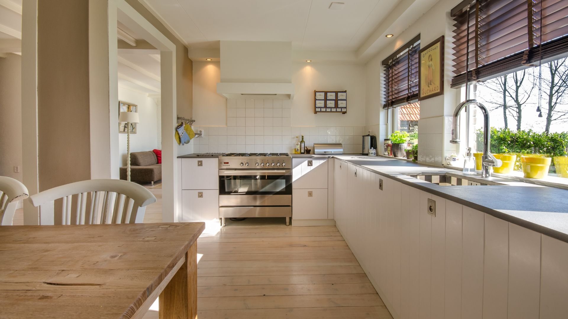 Modern white kitchen with wooden table, stainless steel appliances, and bright windows