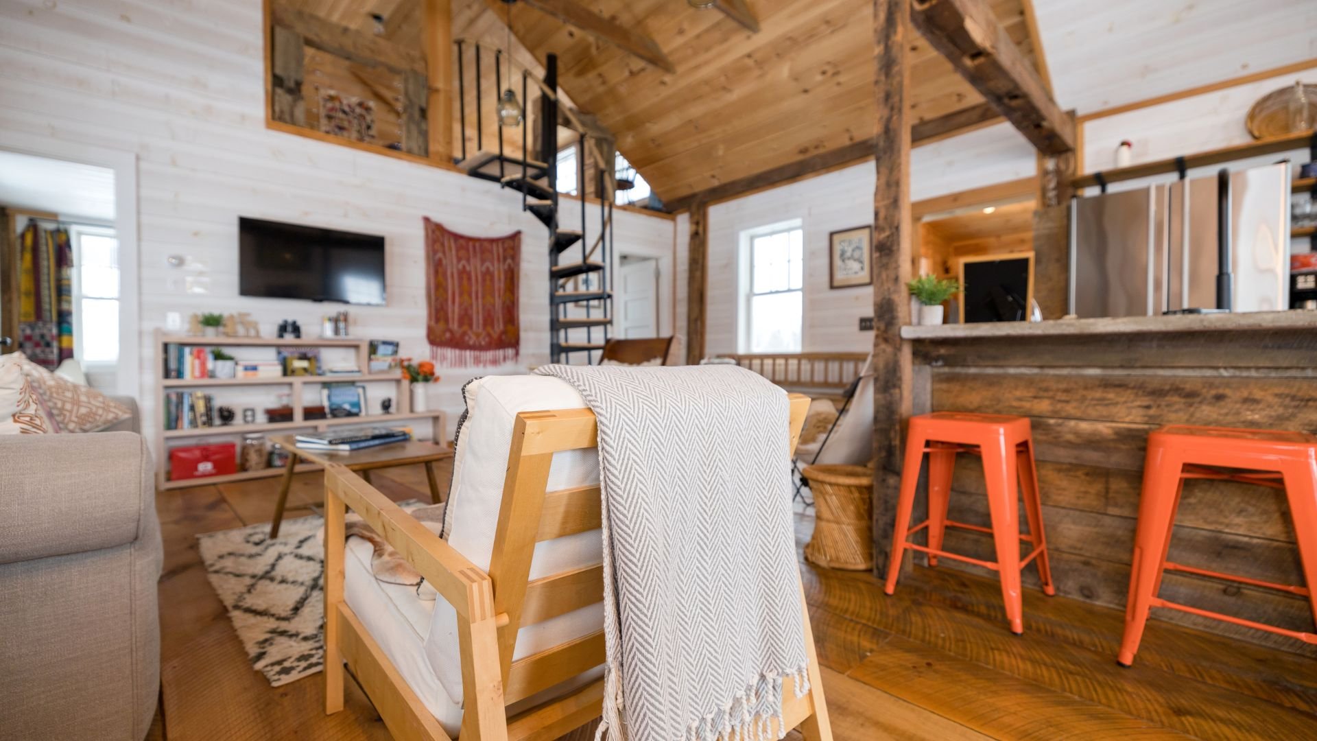 Cozy wooden cabin interior with orange stools and spiral staircase